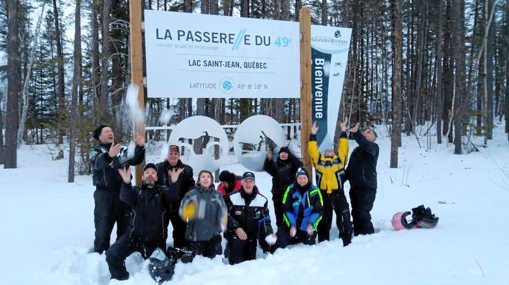 Une partie du groupe de motoneigistes devant l’affiche de La Passerelle du 49e parallèle à Normandin.